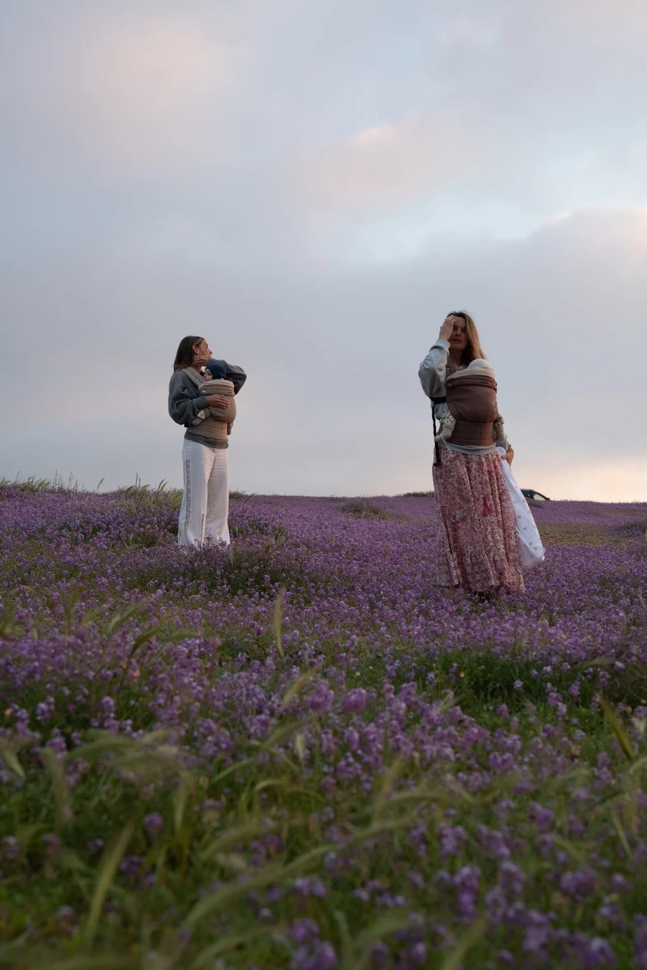 Dos madres llevan a sus bebés en portabebés Babiini en un campo de flores